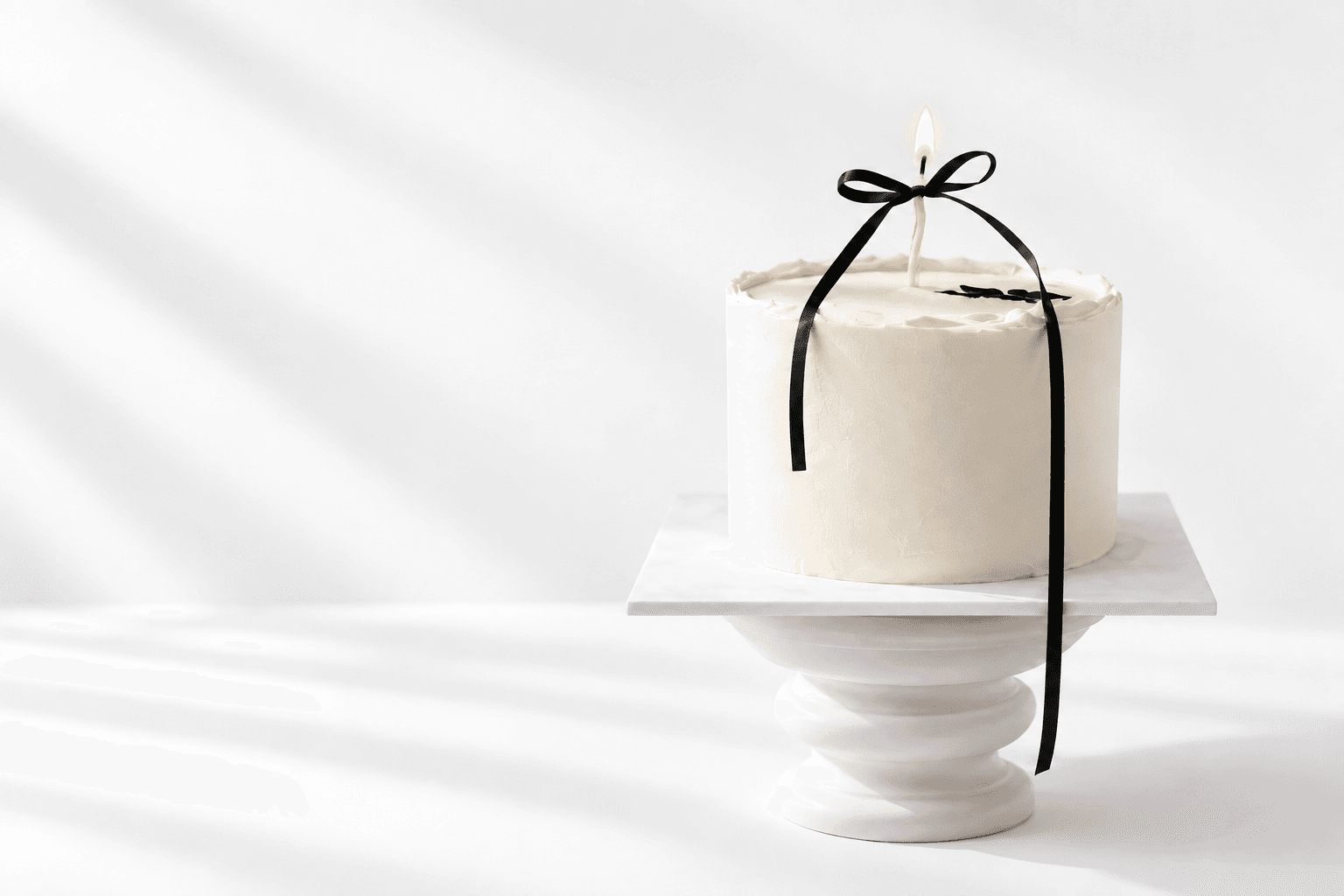 A birthday cake with lit candles on a glass cake stand